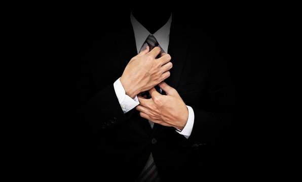 Businessman in black suit tying necktie, on black background