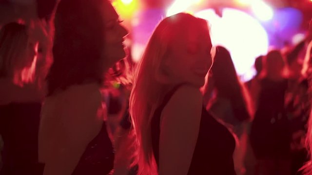 friends dancing in the rays of red spotlights at a disco in a nightclub. girls dancing in a crowd of people
