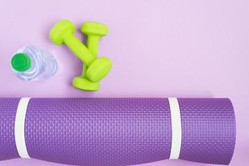 Yoga mat, bottle of water and dumbbells over purple background, top view. Sport concept