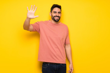 Fototapeta premium Handsome man over yellow wall saluting with hand with happy expression