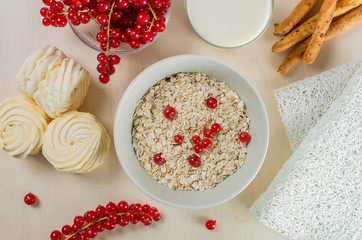 Breakfast served with oatmeal, a glass of milk, bread sticks, cranberry and marshmallow on a wooden background. Flatlay