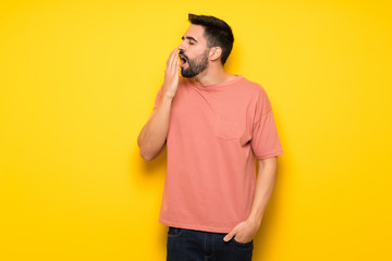 Handsome man over yellow wall yawning and covering wide open mouth with hand