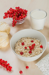 Breakfast served with oatmeal, a glass of milk, cranberry and marshmallow on a wooden background.