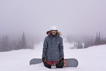 Fototapeta na wymiar Snowboarder girl stading on her knees on top of mountain before she go downhill. Windy blizzard freeride woman