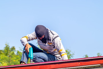 Man is drilling the iron or metal frame for buildinh the roof during house construction with blue sky background. 