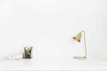 Golden lamp and stationery on white desktop. Minimal interior design concept.