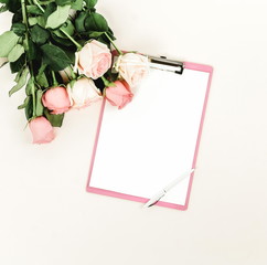 Holiday background.Bouquet of pink roses flowers and clipboard mock up for text  on pale pink background. Festive minimal background. Top view. Copy space