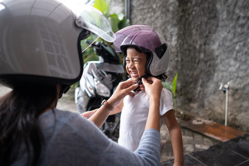 mother help her child to put on a helmet