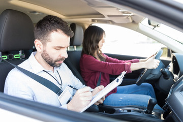 Car Coach Writing On Clipboard While Woman Driving Car