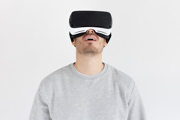 Studio portrait of astonished young man in virtual reality glasses. VR concept