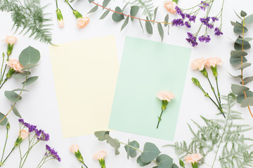 Flowers composition. Paper blank, carnation flowers, eucalyptus branches on pastel  background. Flat lay, top view, copy spaceFlat lay stiil life.