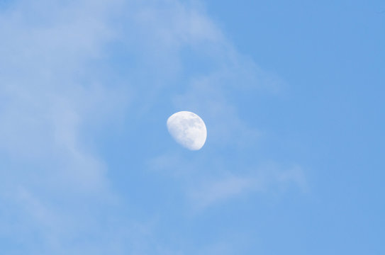 Half bright moon on blue sky background with clouds on day time