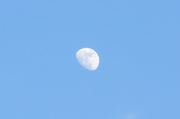 Half bright moon on blue sky background with clouds on day time