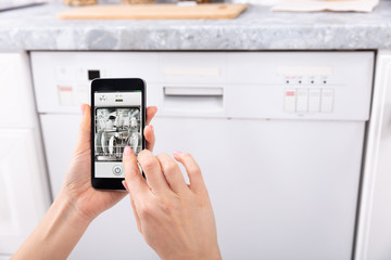 Woman Operating Dishwasher With Mobile Phone