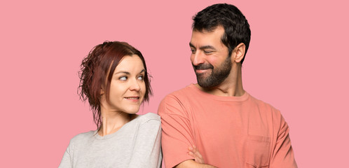 Couple in valentine day keeping the arms crossed looking at each other over isolated pink background