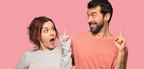 Couple in valentine day intending to realizes the solution while lifting a finger up over isolated pink background