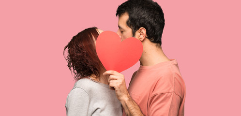 Couple in valentine day holding a heart symbol and kissing over isolated pink background