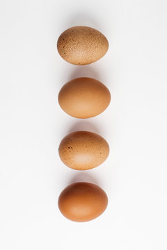 Different brown zwf on a white background lie in a row behind each other. Four chicken fresh delicious eggs in a row.