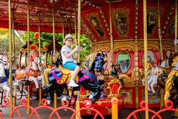 Fototapeta na wymiar Blonde boy in the straw hat and big glasses riding colorful horse in the merry-go-round carousel in the entertainment park