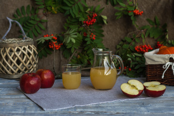 autumn composition with apples and apple juice in a jug with pumkins in basket