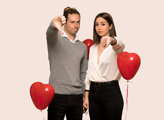 Couple in valentine day showing thumb down sign with negative expression over isolated background