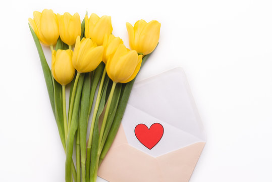 A bouquet of natural, fresh tulips in the composition with an open envelope and paper red heart. Romantic frame with flowers on white isolated background. Wedding or valentine day.