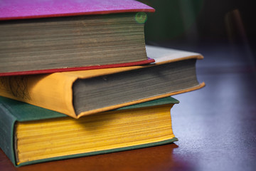 old large books with red, yellow and green covers are on a wooden table