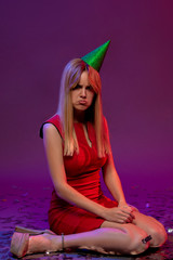 Beautiful girl with blond hair and party hat - unhappy and shocked looks on you . Woman in red dress surprise and sits on the floor. Facial expressions