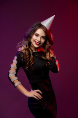 Event, party, Birthday, Christmas or New Year celebrating concept. Young pretty brunette woman in black dress and birthday hat is laughing.. Colorful studio portrait with bright background. Copy space
