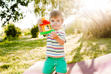 Little cute boy holding a toy house in the garden and looks pensive