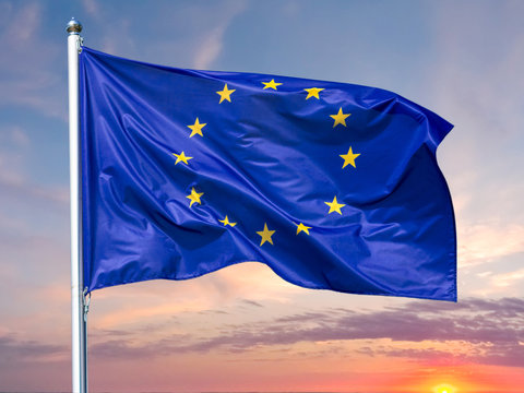 Flag of the European Union waving in the wind on flagpole against background of the sunrise, close-up