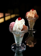 Capa de helado con una bola de fresa y otra de chocolate, nata montada  y una guinda en la parte superior.