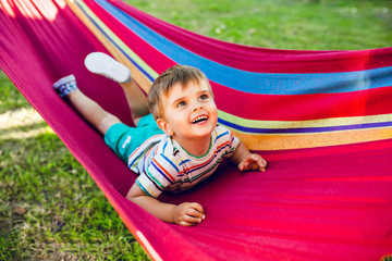 Fototapeta na wymiar Little cute boy resting on bright hammock and having fun. He looks happy