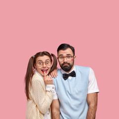 Studio shot of two woman and man geeks look happily, stand closely to each other, isolated over pink background with blank space for your advertising content. Nerd couple after kissing each other