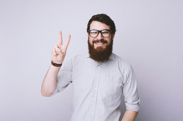 Peace. Bearded man in glasses and shirt is gesturing victory sign