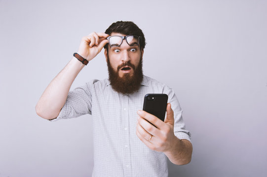 Bearded man using smartphone scared in shock with surprised face with fear expression