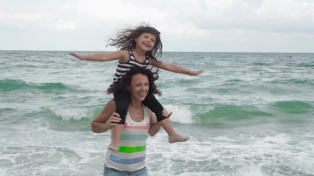 Woman playing with child on the beach. Fly with mom. A little girl sits on her mother's shoulders.