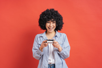 Excited casual young woman playing video games having fun on red background - obrazy, fototapety, plakaty