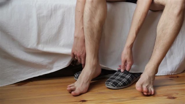 man from the bed becomes on the floor,legs at the bed wear slippers in the morning