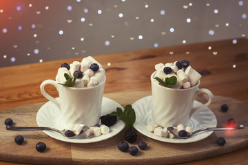 coffee with milk and marshmallows with blueberries and blackberries in white cups on wooden textured background. image