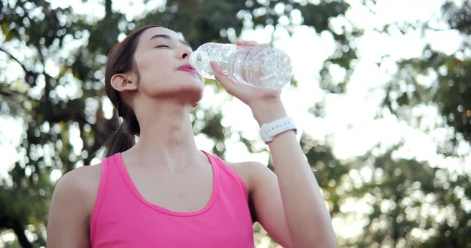 Young beautiful asian woman resting at park. Woman drinking water when exercise finished. People with healthcare, sport and exercise concept.