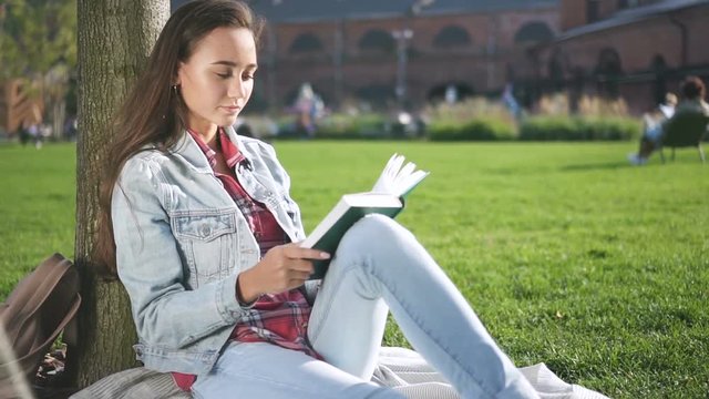 Inspired university student reading book sitting on campus grass. Smart reader learning for final test. Concept of: education, cheerful, entertainment. Portrait.