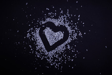 Coconut flakes are scattered in the shape of a heart on a black background. Symbol of love for Valentine's Day. Coconut chips close-up.
