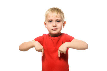 Serious little blond boy in a red shirt stands and shows index fingers down. Isolate on white background.