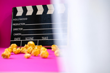 unfocused top view close up black clapperboard and popcorn isolated on bright pink background/ creative movie time concept with copy space 