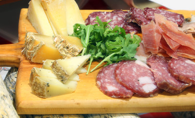 wooden chopping board with cold cuts, cheese and rocket leaves