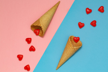 Ice cream waffle cones on pastel pink and blue background, top view, flat lay. Valentine's Day. Many hearts fall out of the waffle cones.