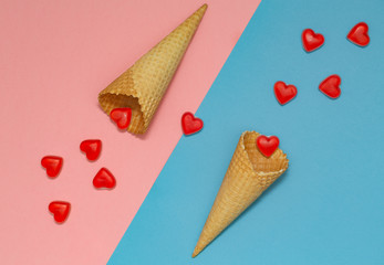 Ice cream waffle cones on pastel pink and blue background, top view, flat lay. Valentine's Day. Many hearts fall out of the waffle cones.