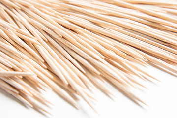 A bunch of unused round toothpicks from light-colored wood arrayed on a white plain background.