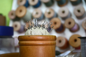 Pins with a round hat in a wooden round box on the background of different threads